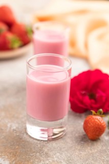 Sweet strawberry liqueur in glass on a gray concrete background and orange textile. side view,
