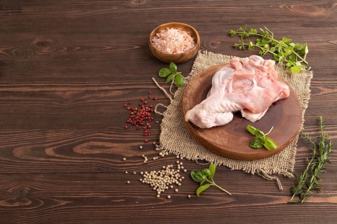 Raw turkey wing with herbs and spices on a wooden cutting board on a brown wooden background and