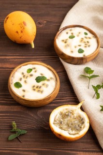 Yoghurt with granadilla and mint in wooden bowl on brown wooden background and linen textile. side