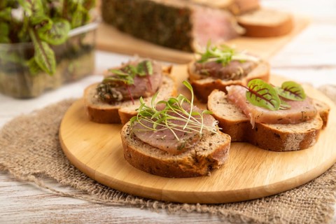 Bread sandwiches with jerky salted meat, sorrel and cilantro microgreen on white wooden background