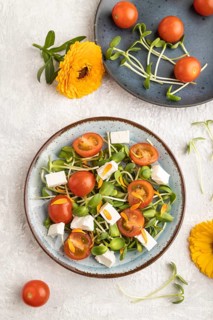 Vegetarian vegetables salad of tomatoes, marigold petals, microgreen sprouts, feta cheese on gray