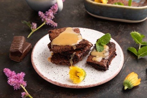 Chocolate brownie with caramel sauce with a cup of coffee on black concrete background. side view,