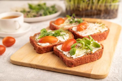 Red beet bread sandwiches with cream cheese, tomatoes and microgreen on gray concrete background.