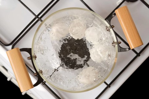 Overhead closeup view of transparent glass saucepan with boiling eggs on a gas stove