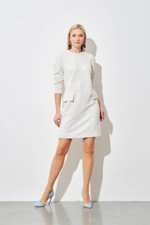 Cute woman in textured white mini dress with pockets and blue heels posing against a white wall