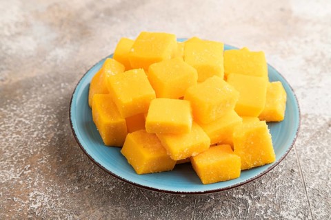 Dried and candied mango cubes on blue plate on brown concrete background. Side view, close up,