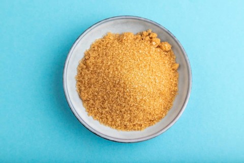 Plate with unrefined golden cane sugar on blue pastel background. top view, flat lay, close up