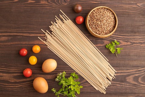 Japanese buckwheat soba noodles with tomato, eggs, spices, herbs on brown wooden background. Top