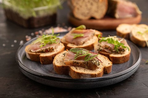 Bread sandwiches with jerky salted meat, sorrel and cilantro microgreen on black concrete