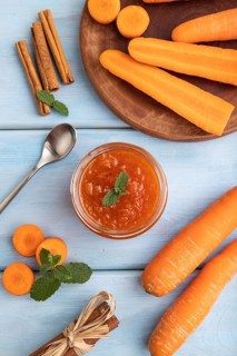 Carrot jam with cinnamon in glass jar on blue wooden background. Top view, flat lay, close up