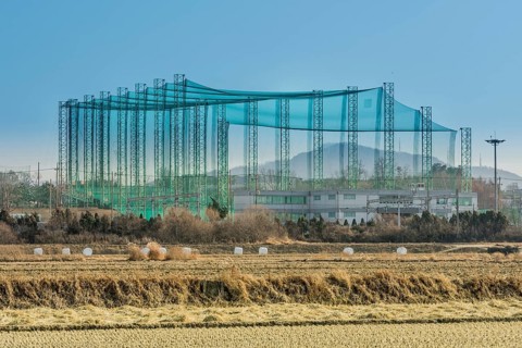 Golf driving range constructed of metal trussed columns and green netting in rural farming