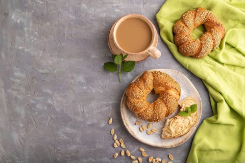 Homemade sweet bun with peanut butter and cup of coffee on a gray concrete background and green