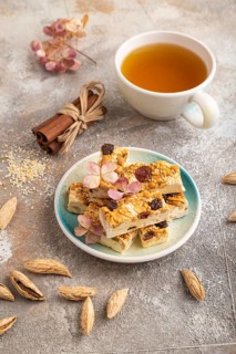 Traditional candy nougat with nuts and sesame with cup of green tea on brown concrete background.