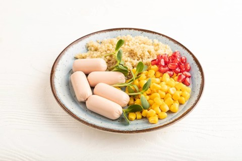 Mixed quinoa porridge, sweet corn, pomegranate seeds and small sausages on white wooden background.