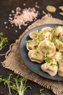 Dumplings with pepper, salt, herbs, microgreen on black concrete background and linen textile. Side