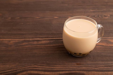 Bubble tea with pistachio and caramel in glass on brown wooden background. Healthy drink concept.