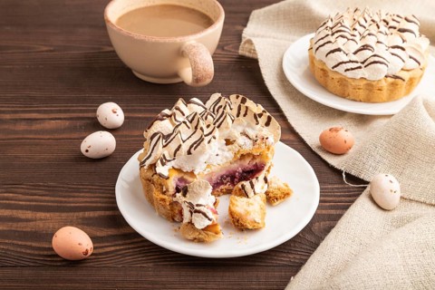 Tartlets with meringue cream and cup of coffee on brown wooden background and linen textile. side