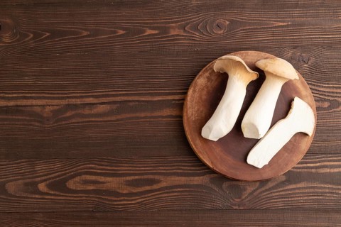 King Oyster mushrooms or Eringi (Pleurotus eryngii) on brown wooden background. Top view, flat lay,