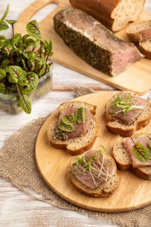 Bread sandwiches with jerky salted meat, sorrel and cilantro microgreen on white wooden background