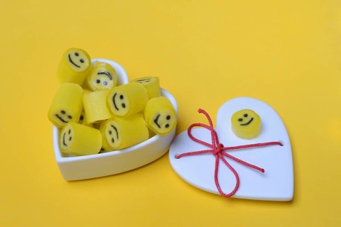 Yellow sweets with smiley in a heart-shaped bowl