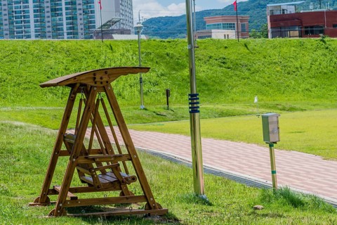 Wooden swing park bench beside walkway with city buildings in background in South Korea
