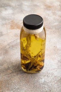 Sunflower oil in a glass jar with various herbs and spices, lavender, sesame, rosemary on a brown