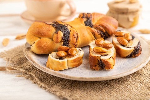 Homemade sweet bun with honey almonds and cup of green tea on a white wooden background and linen