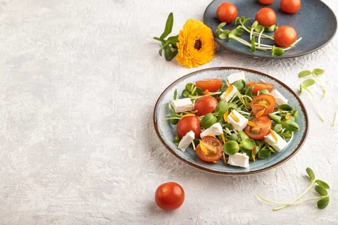 Vegetarian vegetables salad of tomatoes, marigold petals, microgreen sprouts, feta cheese on gray