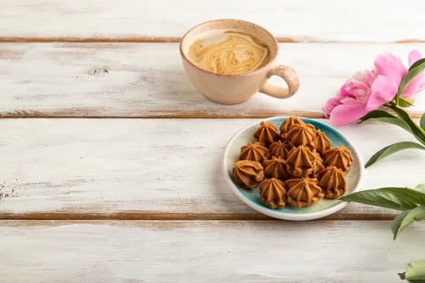 Homemade soft caramel fudge candies on blue plate and cup of coffee on white wooden background,