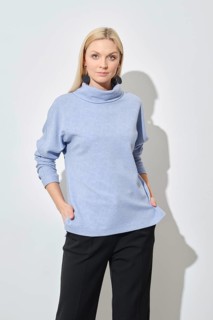 Studio portrait of classy blonde woman in blue sweater and black trousers with her hands in pockets
