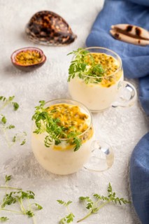Yogurt with passionfruit and marigold microgreen in glass on gray concrete background with blue