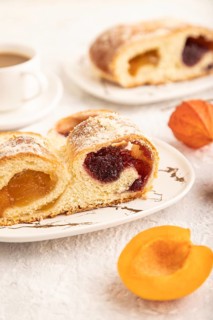 Homemade sweet bun with apricot jam and cup of coffee on gray concrete background. side view, close