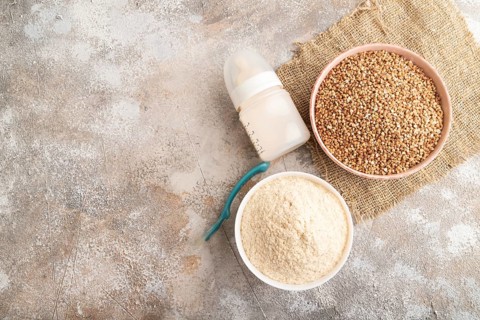 Powdered milk and buckwheat baby food mix, infant formula, pacifier, bottle, spoon on brown