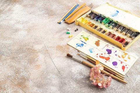 Drawing accessories set: brushes, pencils, watercolor on brown concrete background. Side view, copy