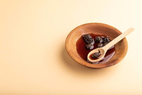 Pine cone jam in wooden bowl on orange pastel background. Side view, copy space
