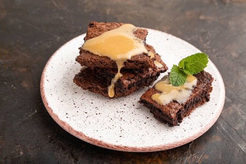 Chocolate brownie with caramel sauce with a cup of coffee on black concrete background. side view,