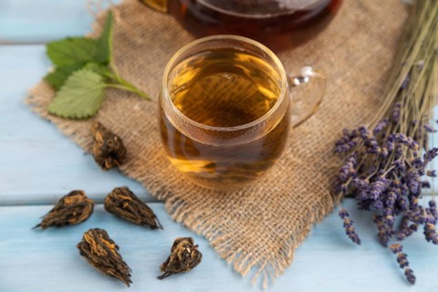 Red tea with herbs in glass on blue wooden background and linen textile. Healthy drink concept.