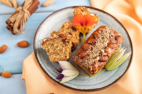 Caramel and almond cake with cup of coffee on blue wooden background and orange linen textile. side