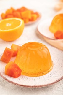 Papaya and orange jelly on gray concrete background and orange linen textile. side view, flat lay,