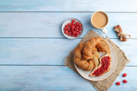 Homemade sweet bun with raspberry jam and cup of coffee on a blue wooden background and linen