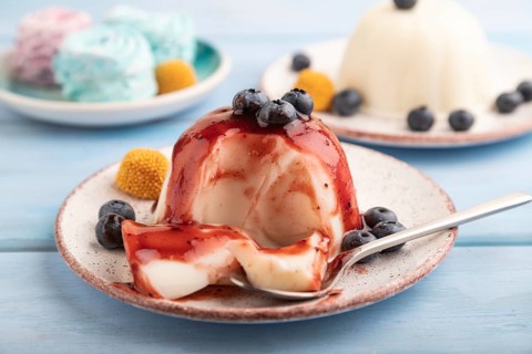 White milk jelly with blueberry jam on blue wooden background and blue linen textile. side view,