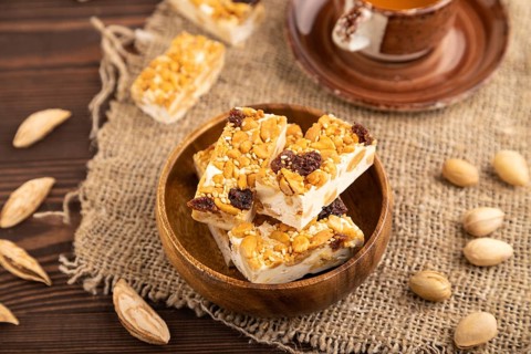 Traditional candy nougat with nuts and sesame with cup of green tea on brown wooden background and