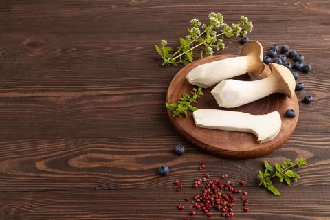 King Oyster mushrooms or Eringi (Pleurotus eryngii) on brown wooden background with blueberry,