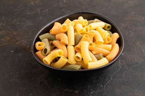 Rigatoni colored raw pasta with tomato, eggs, spices, herbs on black concrete background. Side