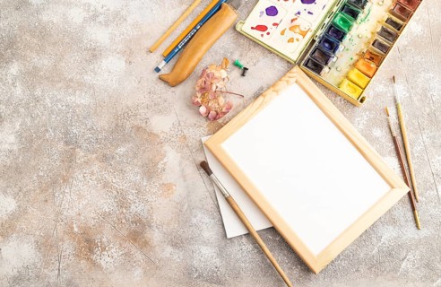 Drawing accessories set: brushes, pencils, watercolor, frame on brown concrete background. Top