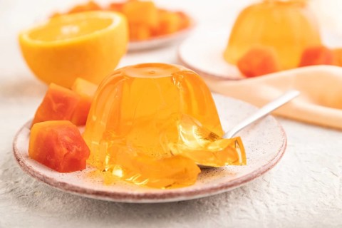 Papaya and orange jelly on gray concrete background and orange linen textile. side view, flat lay,