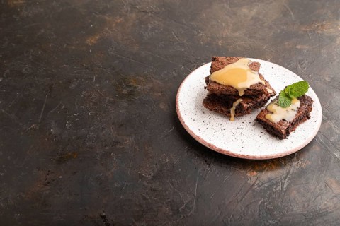 Chocolate brownie with caramel sauce with a cup of coffee on black concrete background. side view,