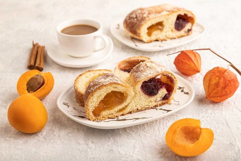 Homemade sweet bun with apricot jam and cup of coffee on gray concrete background. side view, close