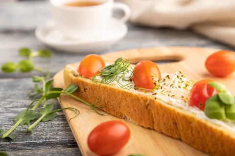Long white bread sandwich with cream cheese, tomatoes and microgreen on gray wooden background and
