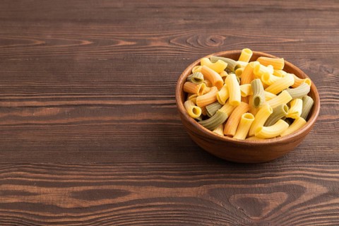 Rigatoni colored raw pasta with tomato, eggs, spices, herbs on brown wooden background. Side view,